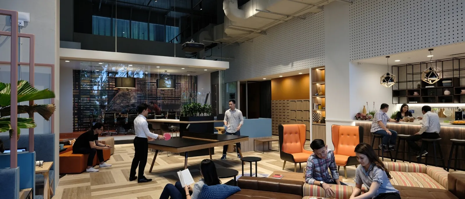 The lounge at Bridge+ Ascent in Singapore: people talking at a long table, reading on sofas and working at the bar.